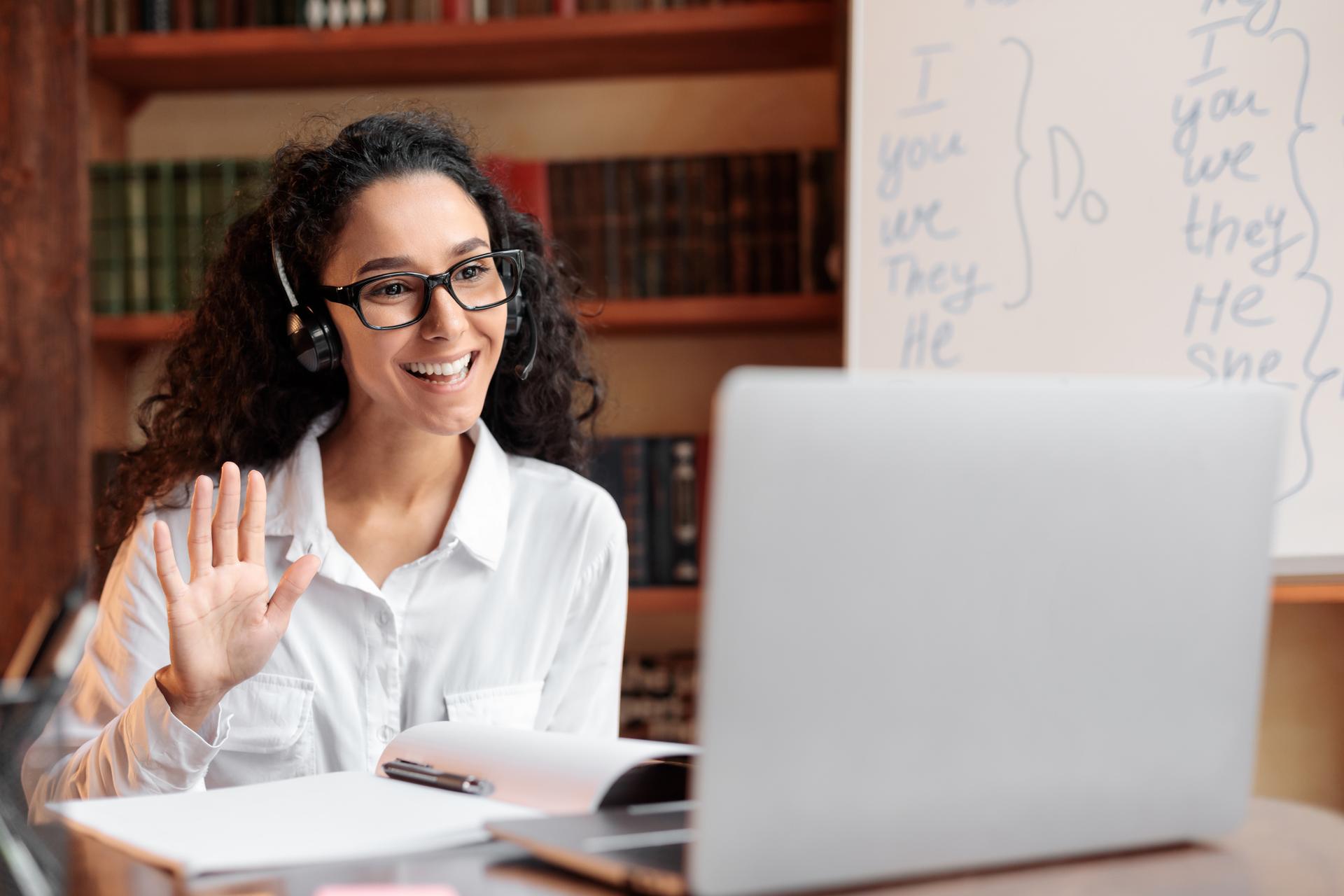 Lady sitting at desk, using computer and waving to webcam