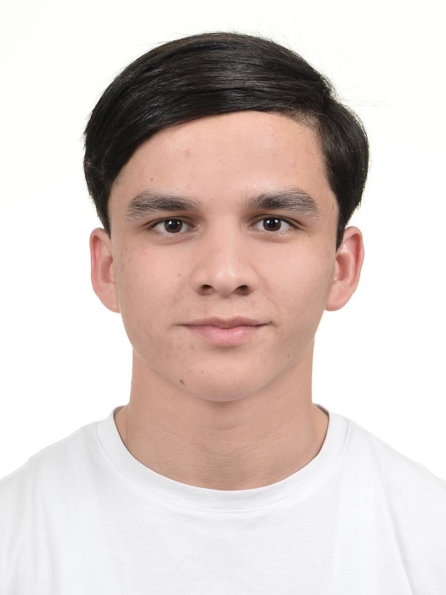 Passport-style photo of a person with short dark hair wearing a white shirt against a plain background.