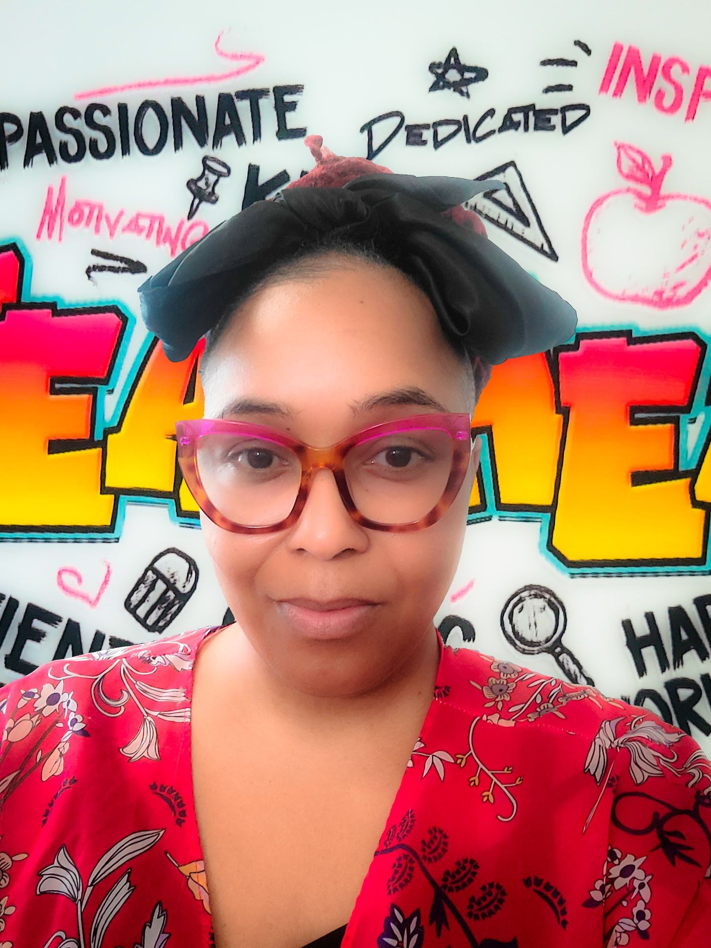 Woman with glasses and headscarf in front of colorful motivational graffiti wall.
