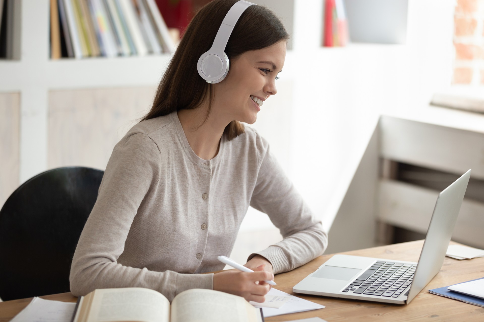 Smiling young female student wearing headset watching educational video.